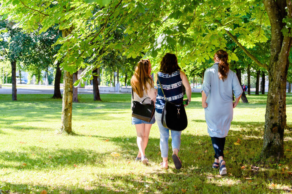 Tre kvinner går gjennom en frodig grønn park.