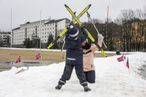 En gutt og en voksen er ute og går på ski i byen. Han holder skiene opp over hodet.