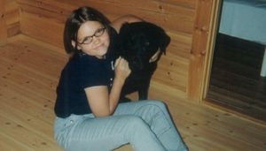 Et bilde av Elisabeth Johnsen Gjetøy da hun var ungdom. Hun smiler mot kamera og holder rundt en svart hund.