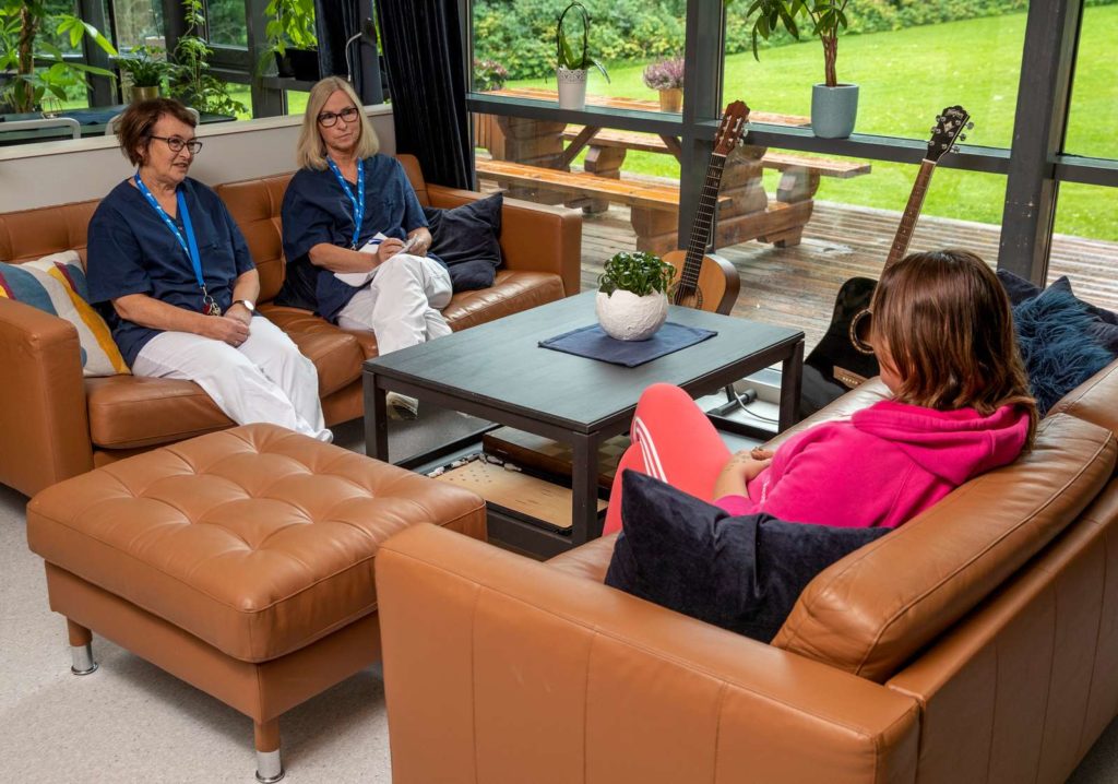 Tre damer sitter samlet i en brun sofagruppe