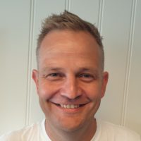Portrettbilde av Johan Kjerstad. Han har en hvit trøye på seg og smiler