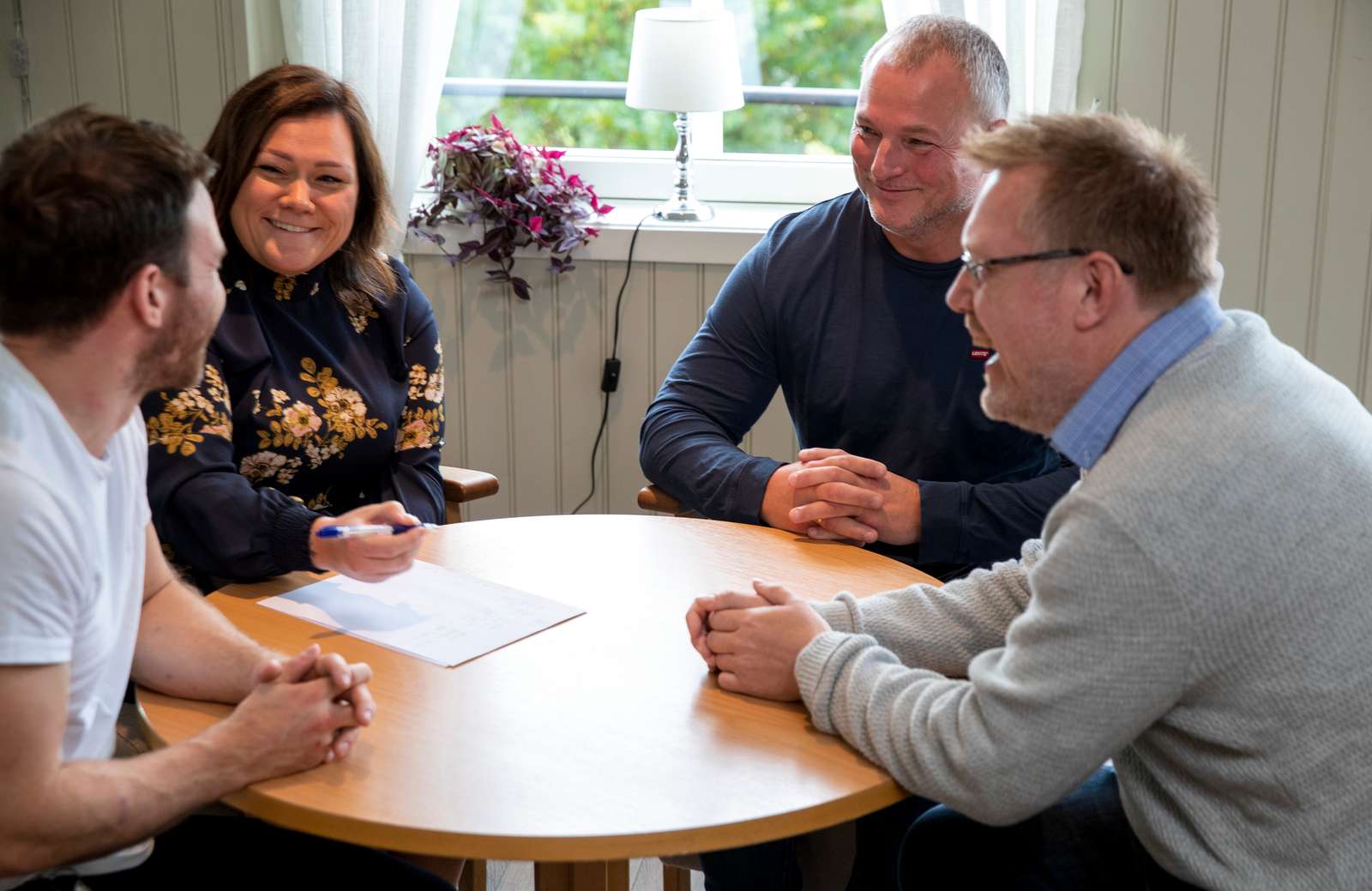 Fire mennesker sitter rundt et bord og har en hyggelig stemning