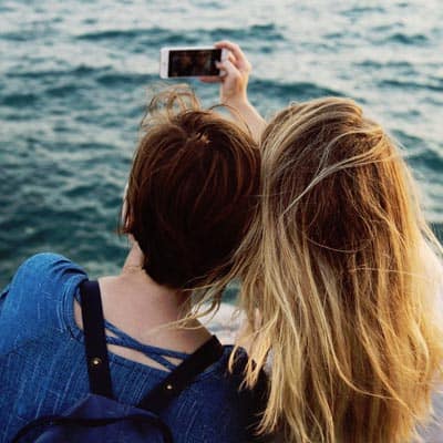 Bakhodene til to jenter som står ved vannet og tar en selfie