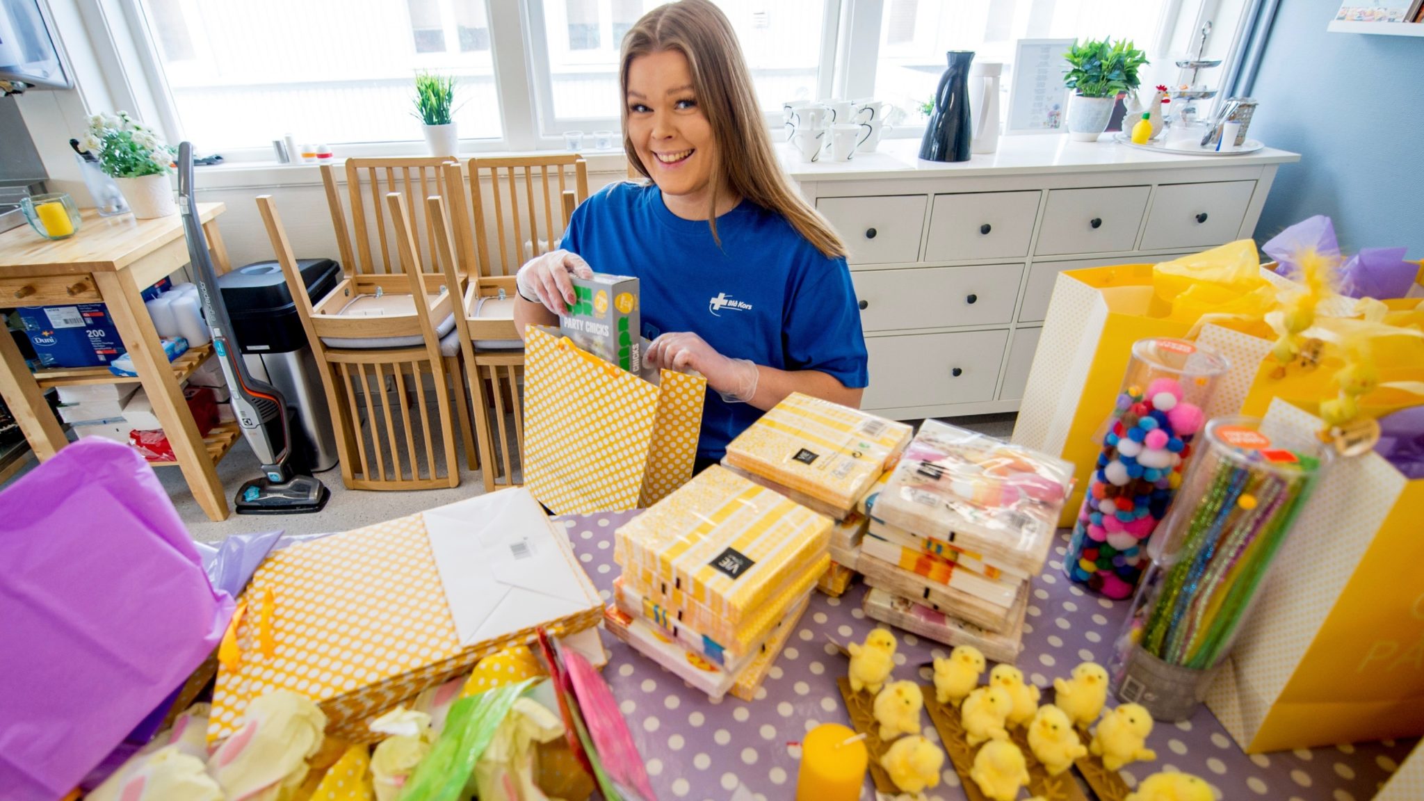 En dame pakker ned i en påskeposer som skal leveres til sårbare familier. På bordet ligger det servietter, lys og mye gøy som familier skal få