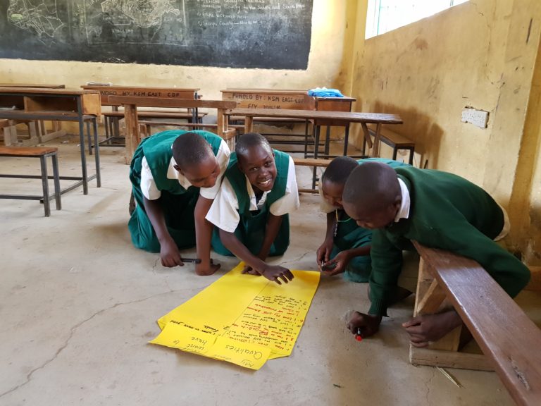 Smilende barn på gulvet i et klasserom i Kenya