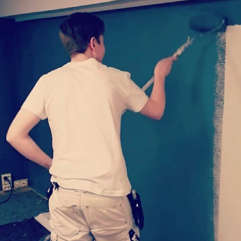 En ung mann som maler en blå vegg. Han har fagbrev som maler fra Blå Kors Rehabil