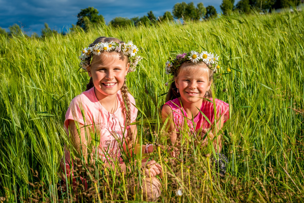 To jenter koser seg i en hveteåker med blomsterkrans på hodet.