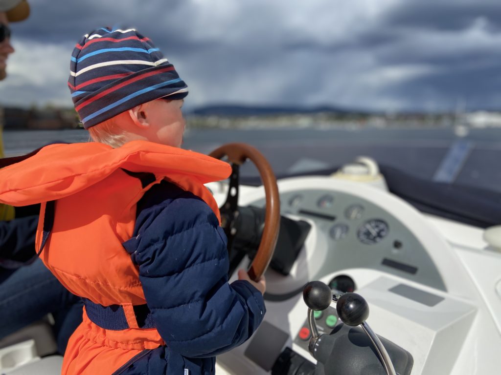 En gutt med en tynn lue på seg er kaptein for båten og styrer rattet