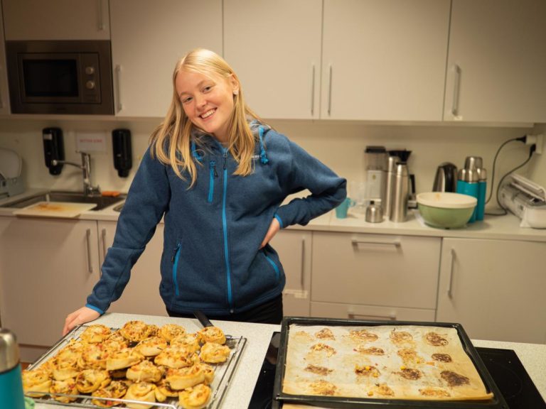 En ung kvinne smiler og står ved et brett med nybakte pizzasnurrer.