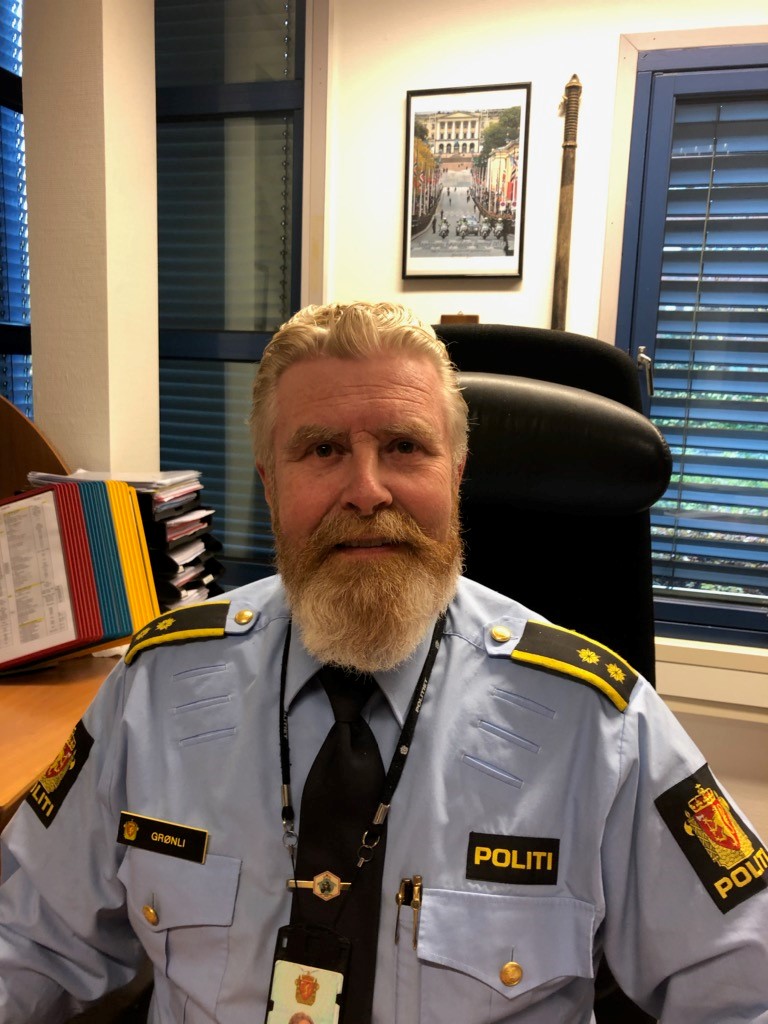 Politimann i uniform som sitter på kontoret og smiler
