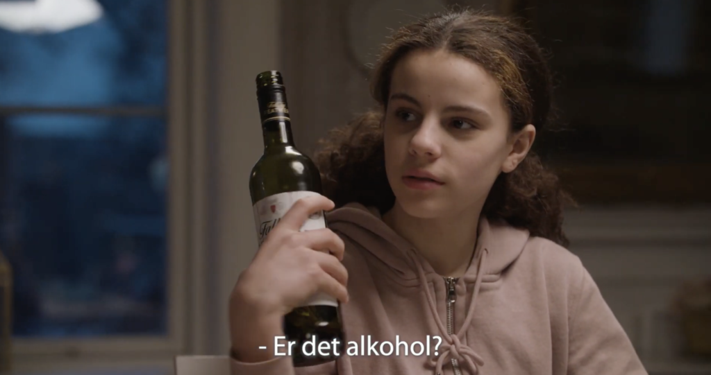 En jente sitter med vinflasken i hånden og lurer på om det er alkohol? Hun er 11,12 år gammel.