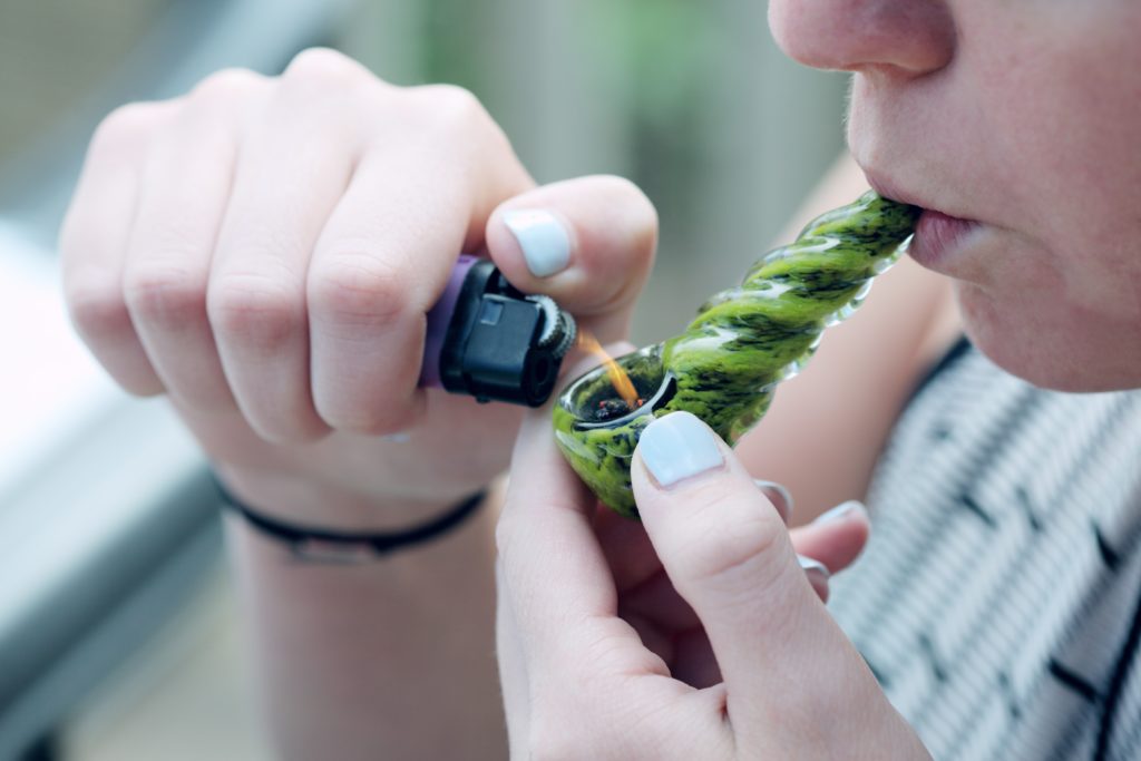 En dame tenner på marijuana-pipen sin med en lighter mens hun halerer inn røyken
