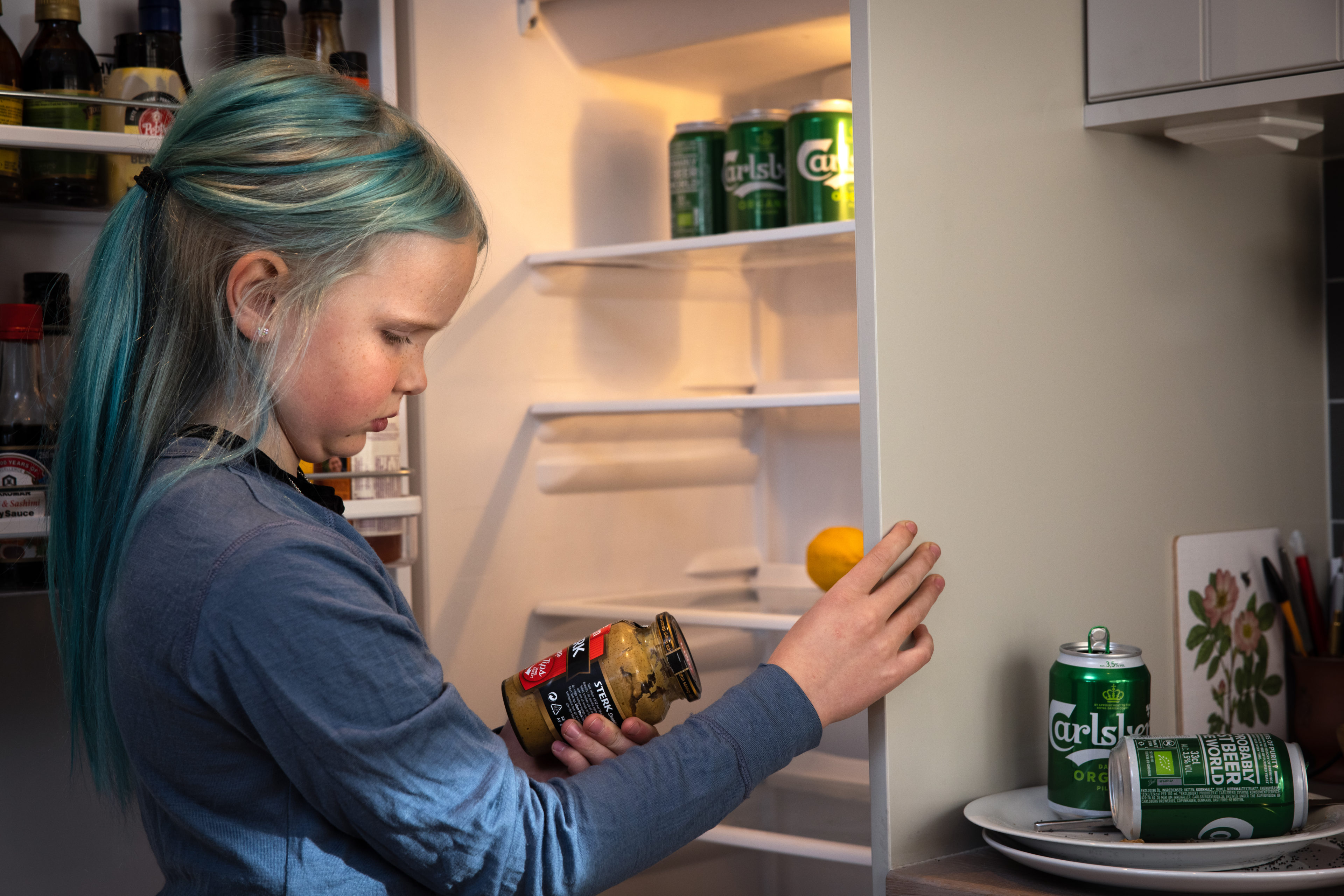 En jente i 10-årsalderen med blått hår leter fortvilet etter mat i et tomt kjøleskap. Kjøleskapet rommer bare øl, sennep og en stakkarslig sitron.