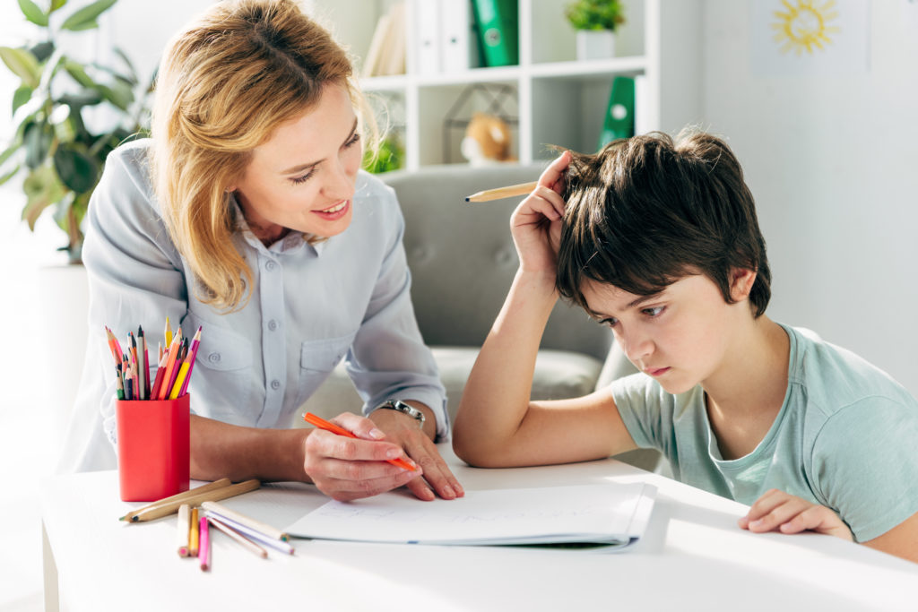 Mor sitter ved bordet og prøver å hjelpe guttungen sin som har dysleksi med skolearbeid.