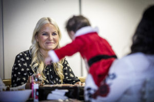 Kronprinsesse Mette-Marit smiler mot en baby med julenissedrakt.