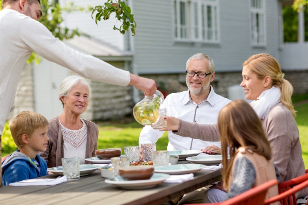 Familie koser seg med drikke ute i hagen på sommeren. 