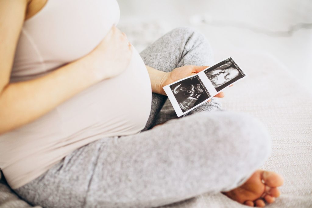 Vi trenger behandlingstilbud for gravide med rusavhengighet. I bildet sitter en gravid kvinne på sengen og ser på ultralyd bilde av foster. 