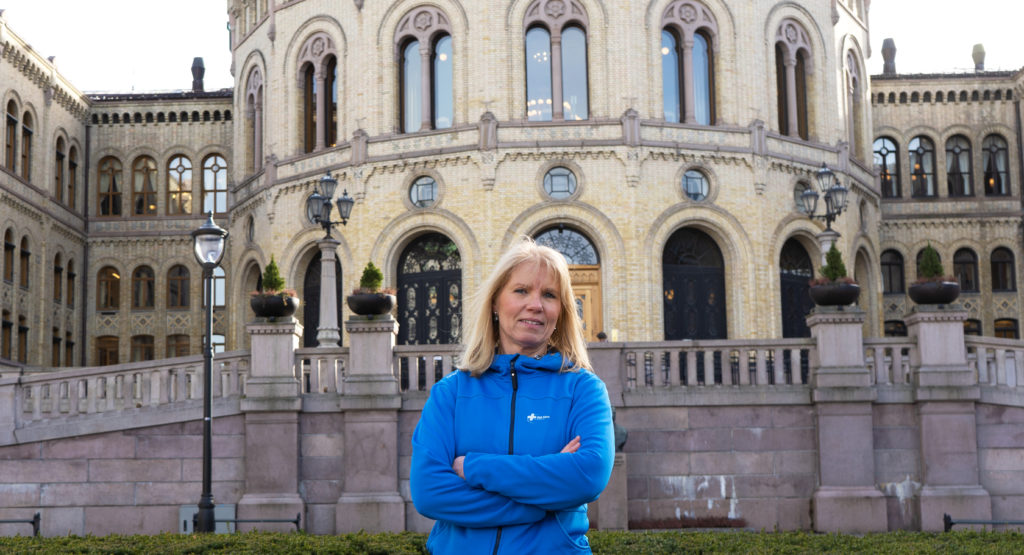 Trine Stensen, Generalsekretær i Blå Kors forann Stortinget for å kommentere statsbudsjettet. Hun står i en blå jakke med logoen til Blå Kors på. Hun er a