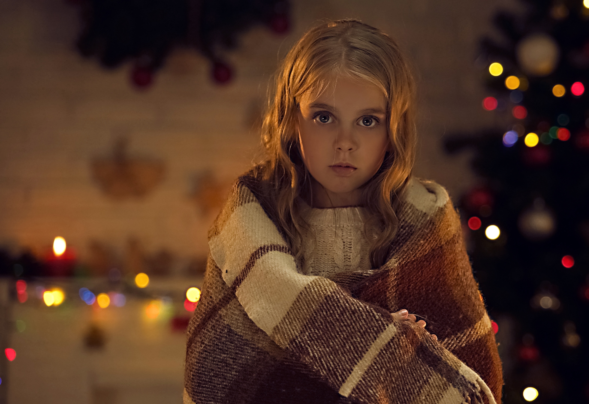 Blå Kors jente med ullpledd står ved et juletre og julelys illustrerer gi gave