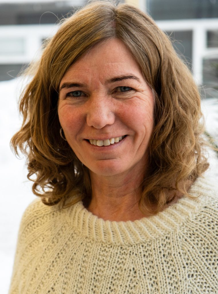 En kvinnelig lærer smiler til kamera. Hun har vært lærer ved Blå Kors videregående skole på Øvrebø i 15 år. Hun har mørkt blondt hår og en en hvit strikkagenser.