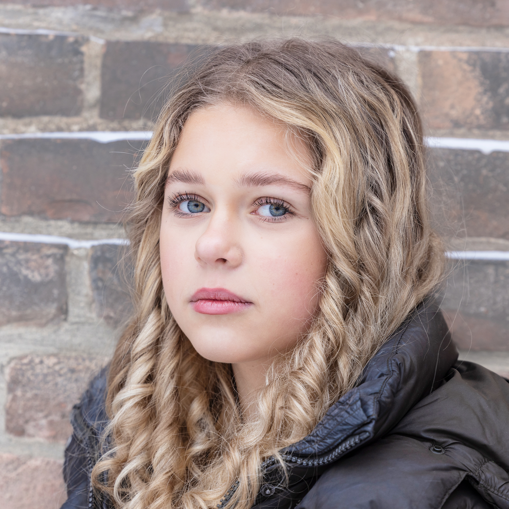 Jente med blondt hår og blå øyne ser inn i kamera.