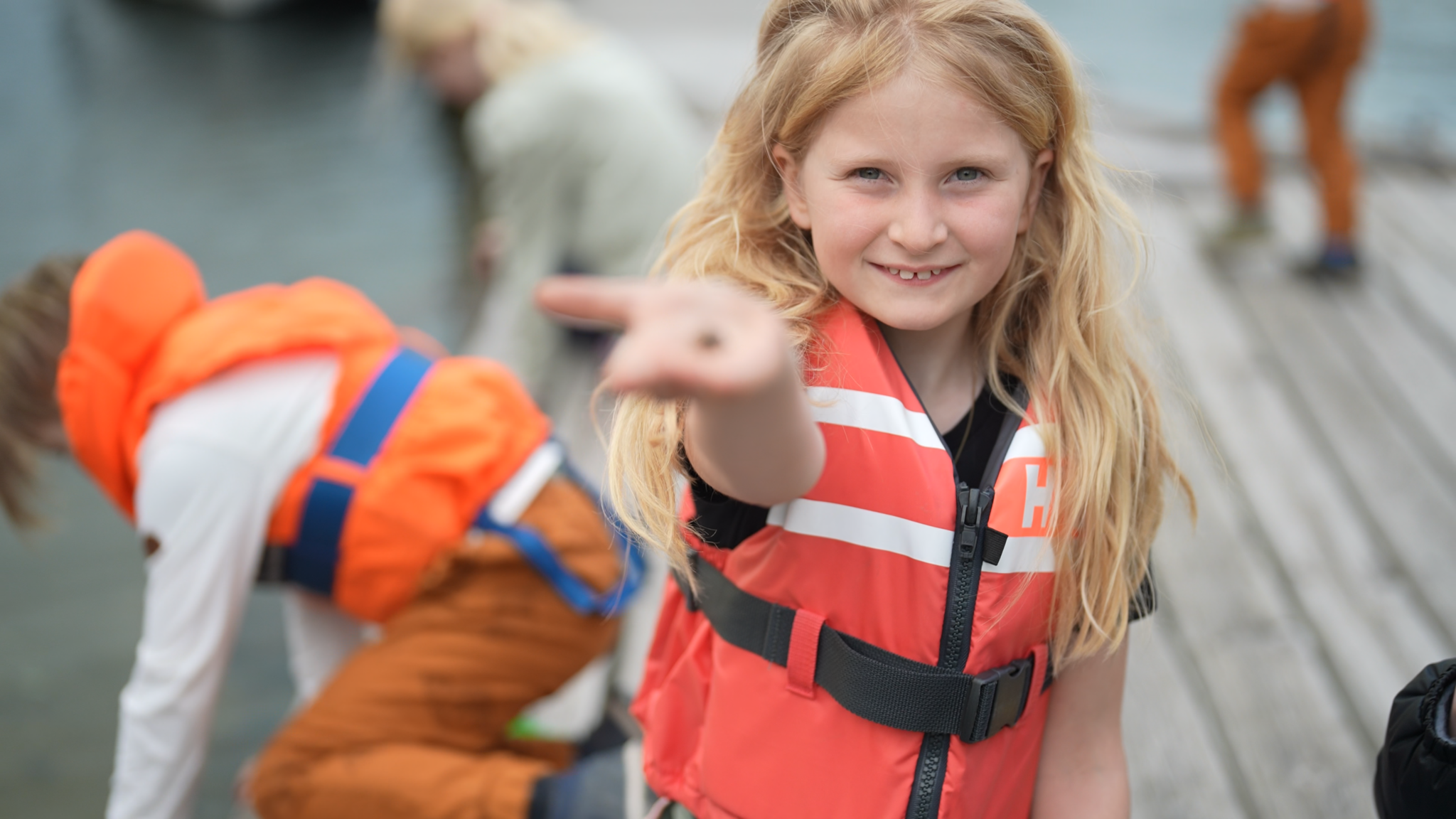 Jente i redningsvest viser frem noe hun har funnet i sjøen