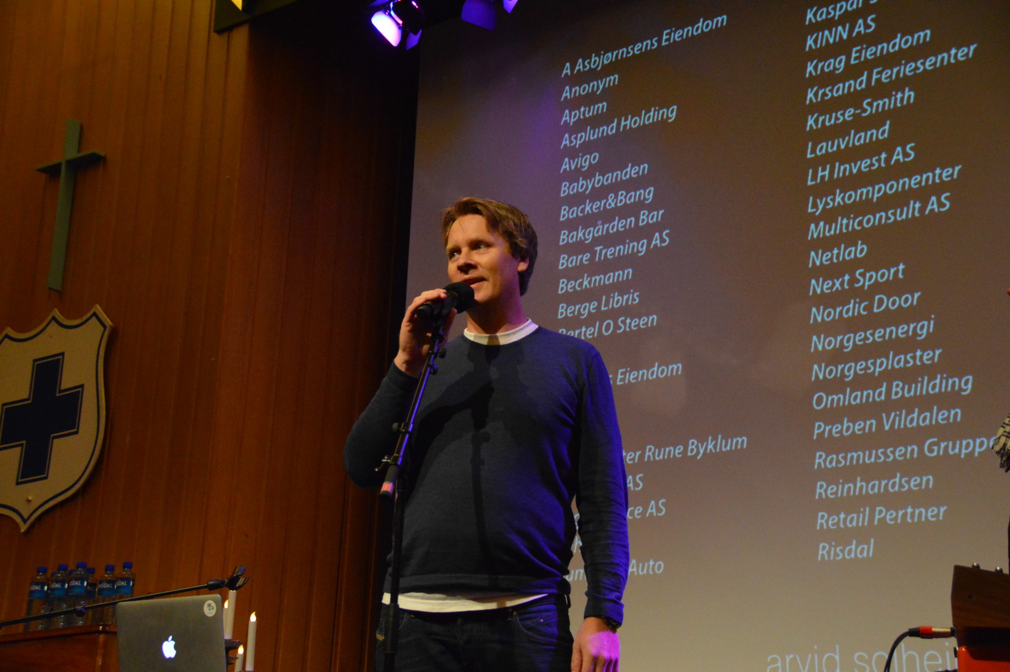 Markedsansvarlig i Blå Kors Kristiansand, Henning Reme, presenterer listen over givere i Storsalen på Blå Kors foran 500 konsertpublikummere.