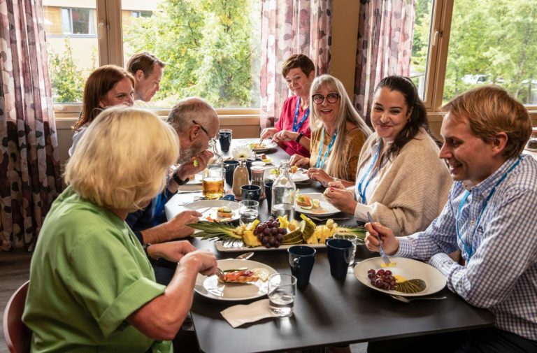 Ansatte hos Blå Kors Lade Behandlingssenter sitter samlet rundt lunsjbordet. De har deilig lunsj med niste og fruktfat