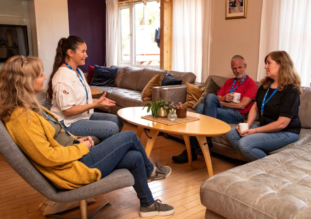 Fire mennesker, tre kvinner og en mann, sitter samlet i en sofagruppe. De drikker kaffe og har det hyggelig sammen