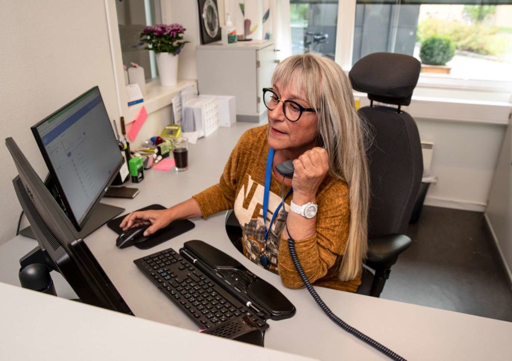 En dame sitter i resepsjonen og holder i en telefon