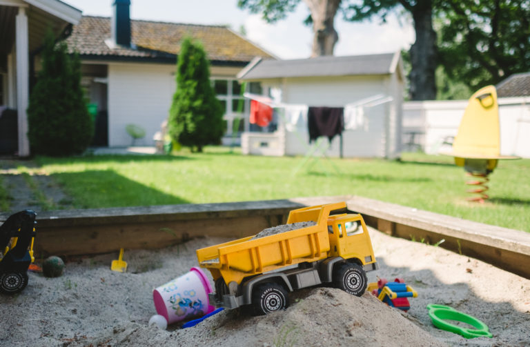 leker i sandkassen med hage og bygninger i bakgrunn