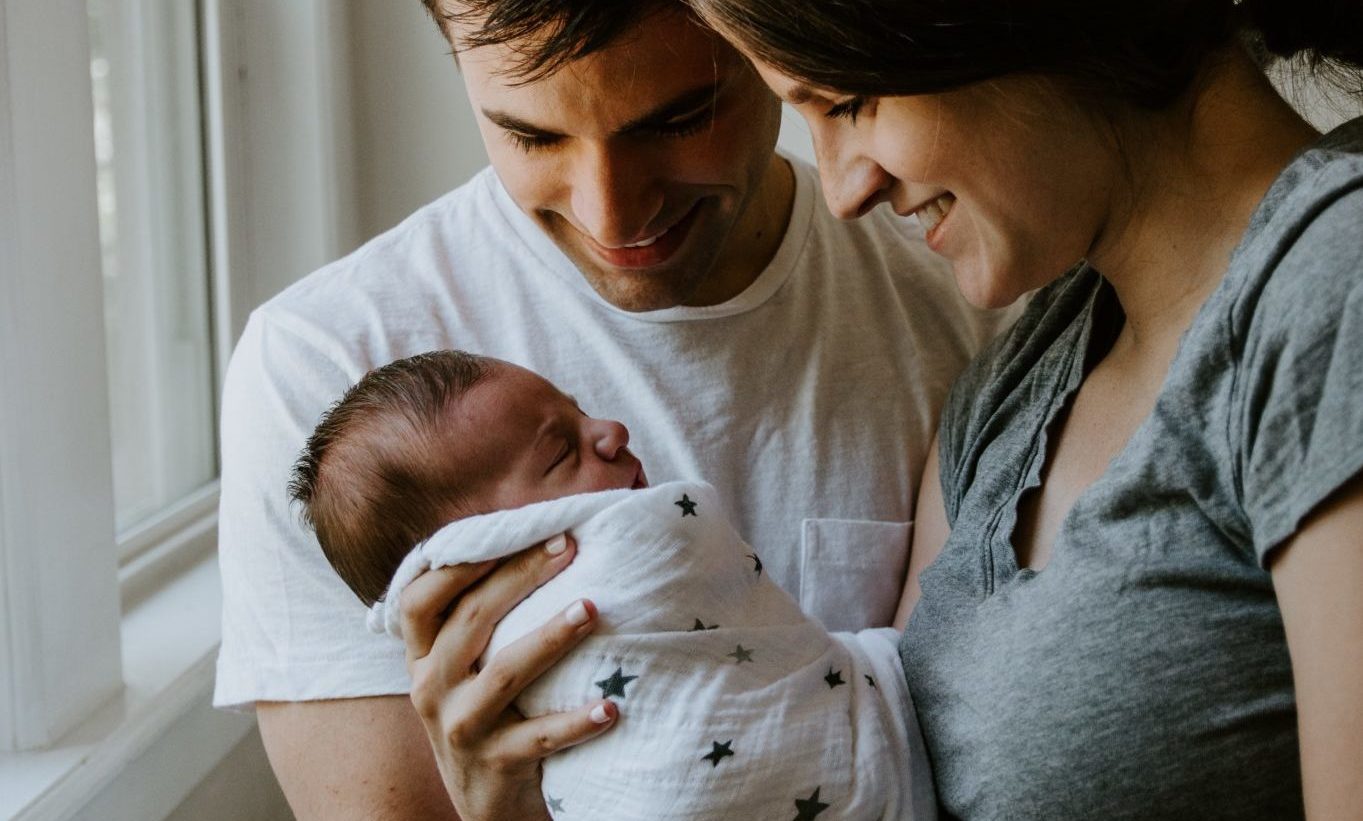 En mann og en dame holder spedbarnet sitt i armene og smiler
