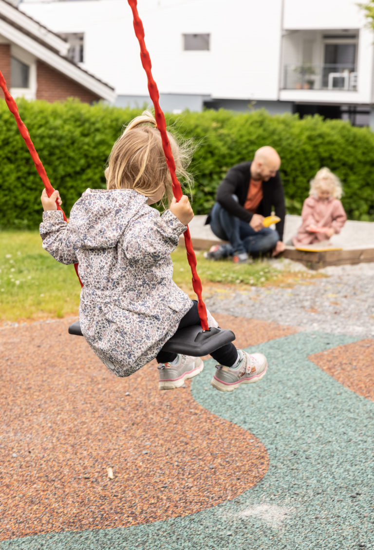 Et barn husker mens en mann og et annet barn sitter ved sandkassen