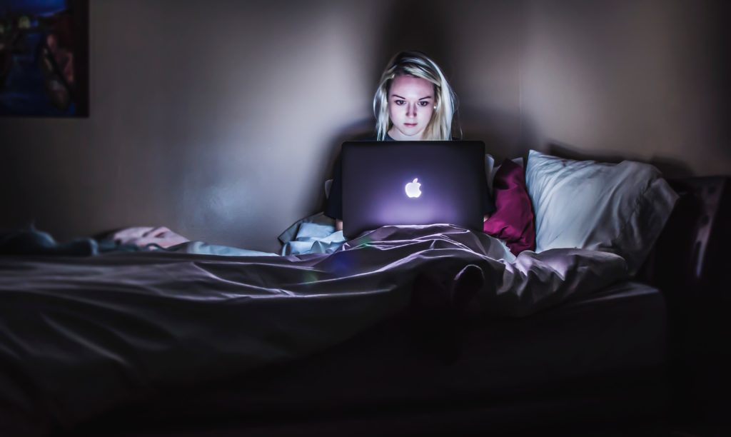 Ung kvinne sitter i sengen sin med Macen på fanget og ser på noe i mørket