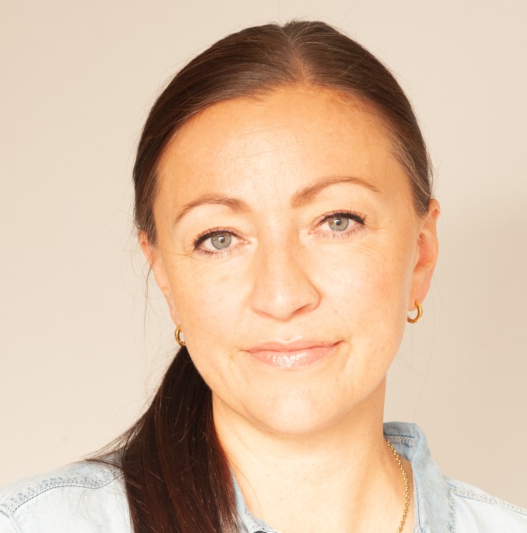 Kvinne med mørkt hår i hestehale som smiler litt