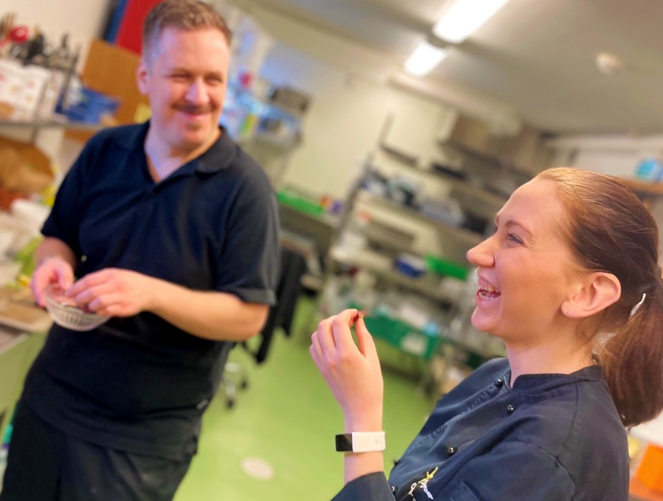 en kvinne og en mann smiler og spiser på kjøkkenet