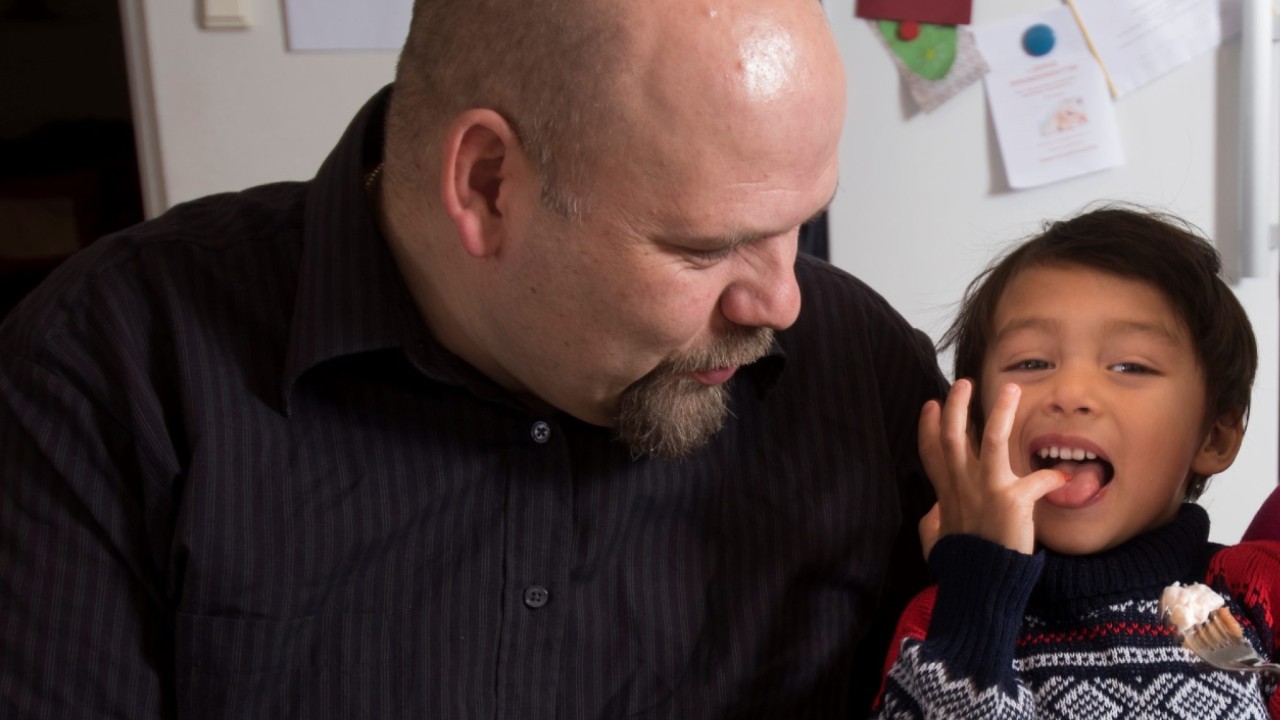 En mann som smiler og holder rundt en gutt. Gutten slikker på fingrene sine og ser fornøyd ut