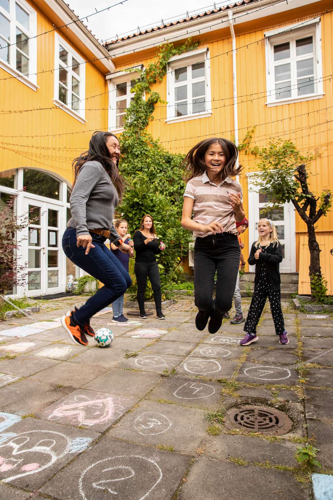 Barn og voksne leker ute i gården foran Barnas Stasjon.