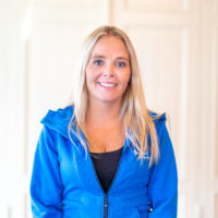 Kvinne med lyst langt hår smiler. Hun har på seg en blå Blå Kors-genser